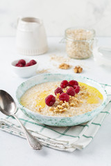 Oatmeal porridge with fresh raspberries, walnuts and butter in a ceramic plate on a light stone or concrete background. Selective focus.
