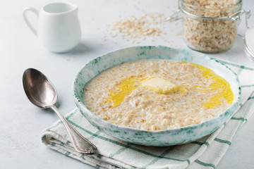 Oatmeal with butter in a ceramic plate on a light stone or concrete background. Selective focus.