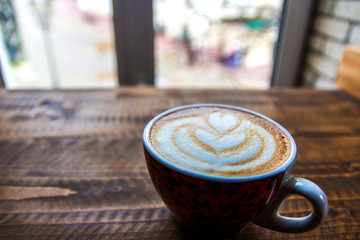 Cup of coffee with pattern on milk foam on a wooden table near the window
