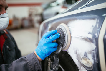 Car detailing - Man with orbital polisher in auto repair shop polishing car. Selective focus on man's hand and polisher. 