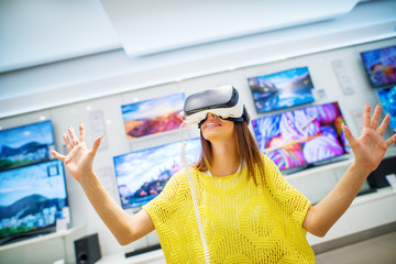 Confused happy young attractive woman tasting VR and with open hands exploring space in a tech store.