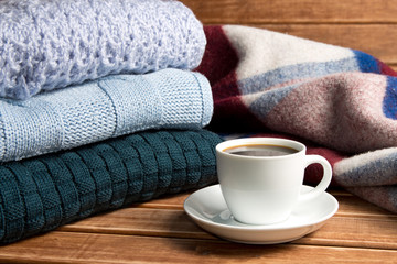 Fototapeta na wymiar Stack of cozy knitted warm sweater and a blanket . Sweaters in retro Style and a Cup of coffee. The concept of warmth and comfort.