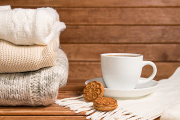 Stack of cozy knitted warm sweater , wooden background . Sweaters in retro Style and a Cup of hot chocolate. The concept of warmth and comfort.