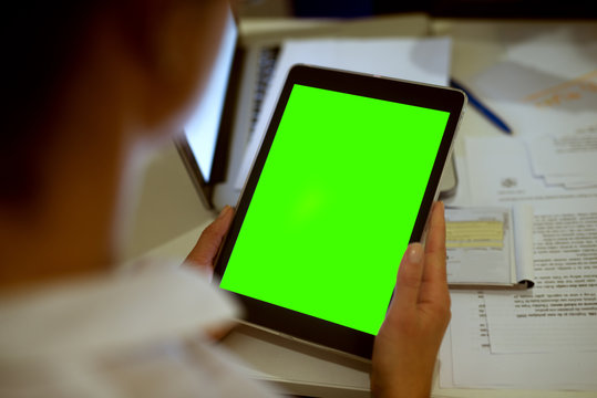 Rear view of blurred woman holding a tablet with a blank editable green screen.