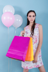 Beautiful young girl in a flower dress holding balloons and gift bags on a blue background