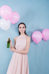 A young girl in a flower dress standing surrounded by balloons and held a green bottle