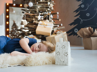 The child sleeps on New Year's Eve next to the Christmas tree and waits for gifts and wonders from Santa Claus. Merry Christmas and Happy New Year. Cute baby sleeping, christmas decoration around him.