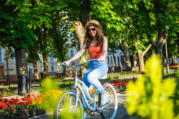 Obraz premium Young beautiful woman riding on bicycle in summer park. Green trees background 