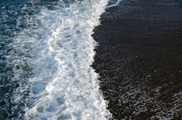 Sea wave with foam against a background of dark sand. Top view.