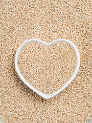 Quinoa in heart-shaped bowl on quinoa background