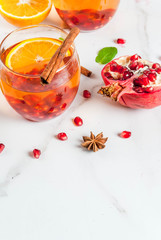 Fall and winter drinks. Warm refreshing cocktail with  pomegranate, oranges, cinnamon, spices and mint. On a white marble table. Copy space
