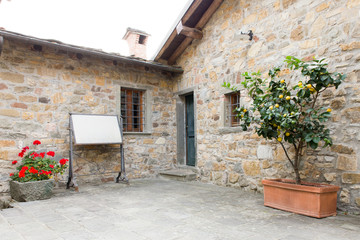 An ancient building in a tuscany little town with a plant of lemons and a white blackboard in front of the door