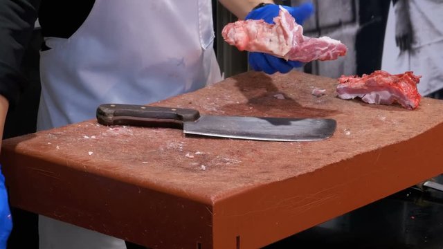 Butcher Cutting Raw Meat With Big Knife in the Market of La Boqueria. Barcelona. Spain. Butcher cuts of beef meat at the market. A man in gloves cuts fresh, juicy beef meat on a wooden board.
