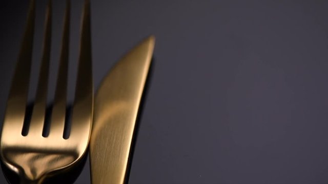 Luxury golden cutlery closeup. Knife and fork over black background. Rotation 360 degrees. 4K UHD video