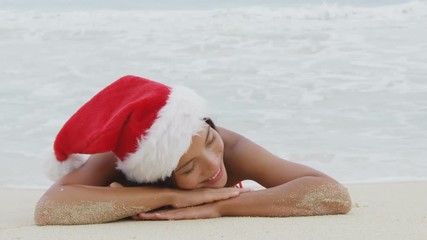 Christmas beach woman wearing santa hat and bikini on holidays travel vacation getaway travel relaxing on tropical beach lying in the sand. Beautiful young female model.