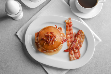 Plate with tasty pancakes and bacon on table