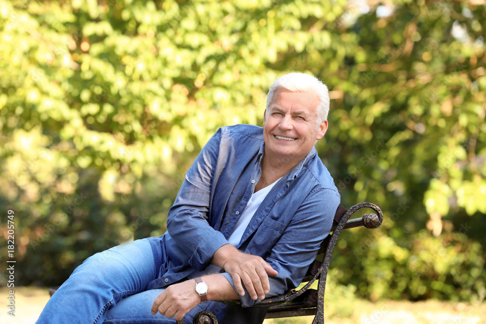 Wall mural Handsome mature man sitting on bench in park