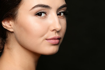 Fototapeta premium Beautiful young woman with eyelash extensions on dark background