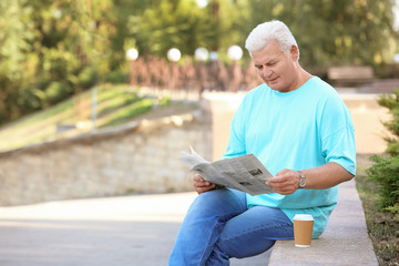 Obraz premium Handsome mature man with newspaper in park