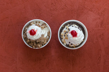 Two ice cream sundaes with cherry on top over red wood