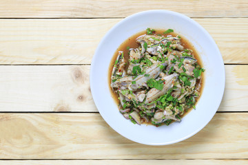 Fresh sardinella fish of spicy salad in white dish on wooden floor.