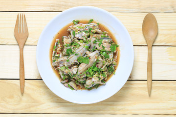 Fresh sardinella fish of spicy salad in white dish on wooden floor.