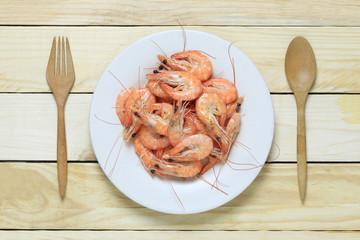 Boiled sea shrimp in white dish on wooden floor.