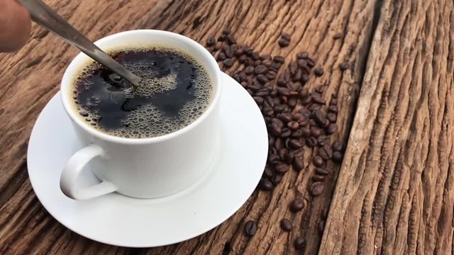man hand stir coffee in white cup with spoon on wooden background, slow motion action