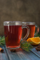 Tea in a glass mug, cinnamon stick, orange and fir branch.