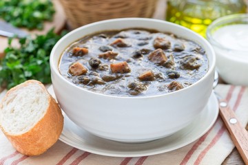 Black bean and ham soup in ceramic bowl on wooden table, horizontal