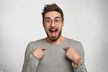 Is it really I? Excited overjoyed male reacts actively on winning competition, points at himself,...