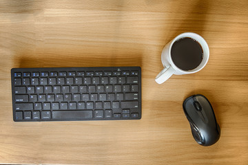 Computer workplace, top view: keyboard, mouse and a cup of black coffee on a wooden table. HDR image