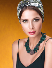 Hairstyle with headscarf. Portrait of young beautiful woman with necklace on her neck. Golden neutral background