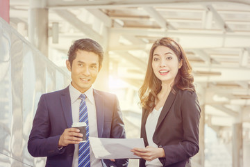 Close up of Happiness businessman with coffee cup and business woman with sheet in hand blurred city background, Success team concept.