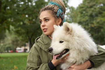 a young woman in a green coat and with dreadlocks on her head resting with her Samoyed dog in the...