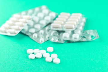 Full and empty packs of white capsules and pills packed in blisters with copy space on aquamarine background. Focus on foreground, soft bokeh