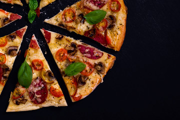 Hot and delicious pizza with salami tomatoes cheese and mushrooms ready to eat on a black wooden background. Top view.