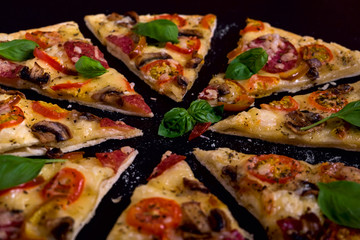 Hot and delicious pizza with salami tomatoes cheese and mushrooms ready to eat on a black wooden background.
