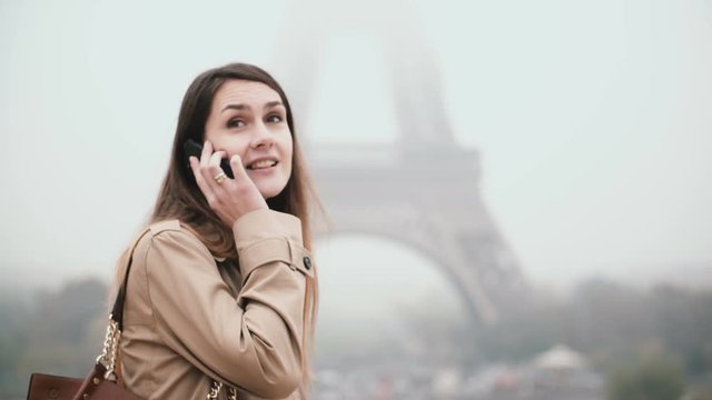 Young beautiful woman walking in downtown near the Eiffel tower in Paris, France and talking on mobile phone.