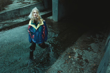 dystopian fashion portrait of model in river of sewage against entrance to tunnel which leads under...