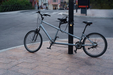 Double bike tandem is tied to the pole with a padlock.