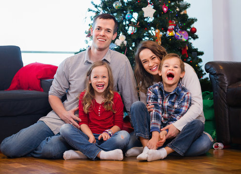 Young happy family sitting by Christmas tree at home