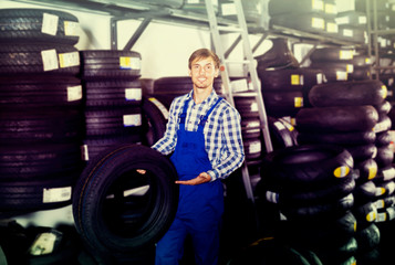 young cheerful mechanic man working with car tires in workshop