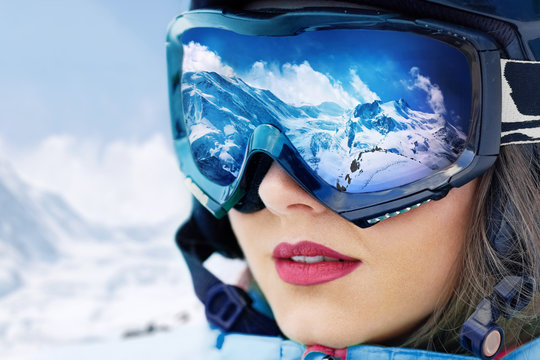 Portrait of young woman at the ski resort on the background of mountains and blue sky.A mountain range reflected in the ski mask