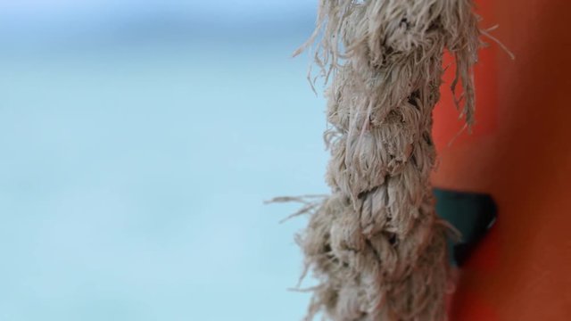 A macro shot of a ragged rope. The shot then blurs the rope and focuses in the background. A crystal blue sea is in the background.