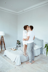 The young couple embraces and kisses in the morning in the bedroom. The man and the woman in house...