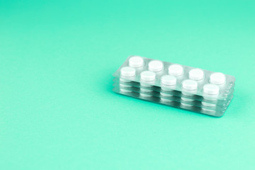 Packs of white pills packed in blisters with copy space on aquamarine background. Focus on foreground, soft bokeh