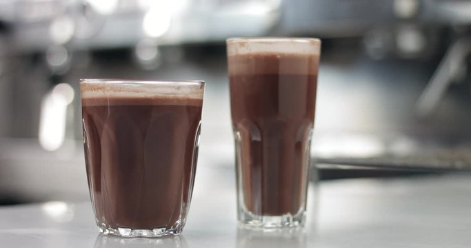 Close up of a barista in an industrial looking cafe making hot cocoa drinks in glass tumblers