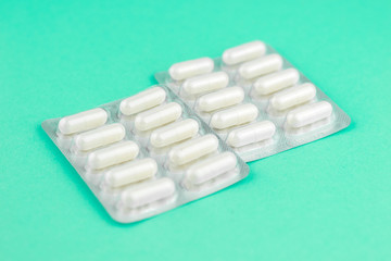 Packs of white capsules packed in blisters with copy space on aquamarine background. Focus on foreground, soft bokeh