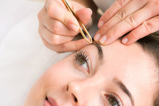 Kosmetikstudio Augenbrauen werden von Hand mit Pinzette bei junger Frau gezupft